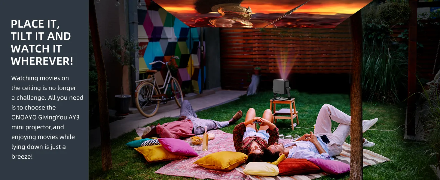 Friends lying on cushions in a garden watching a film projected onto the canopy above them by the ONOAYO AY3